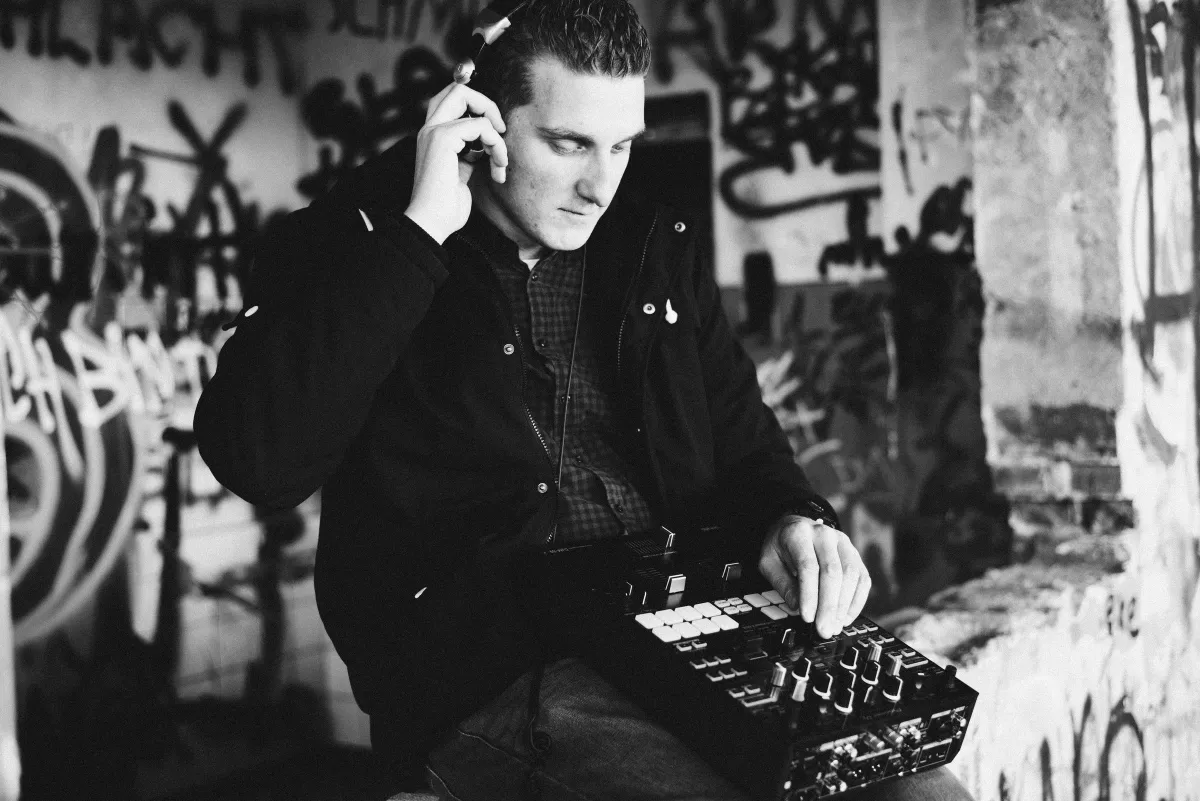 Schwarz-Weiß-Foto: DJ EMC mit Kopfhörern bedient einen DJ-Controller vor einer Graffiti-Wand