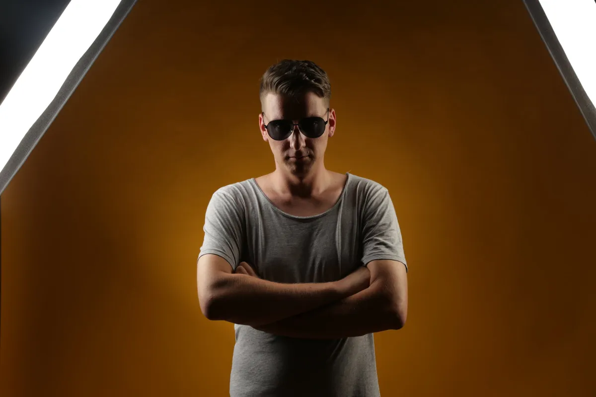 DJ EMC mit Sonnenbrille und verschränkten Armen vor orangem Studiohintergrund