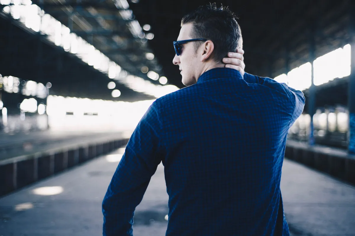 DJ EMC im blauen Hemd mit Sonnenbrille in einer leeren Bahnhofshalle, von hinten fotografiert