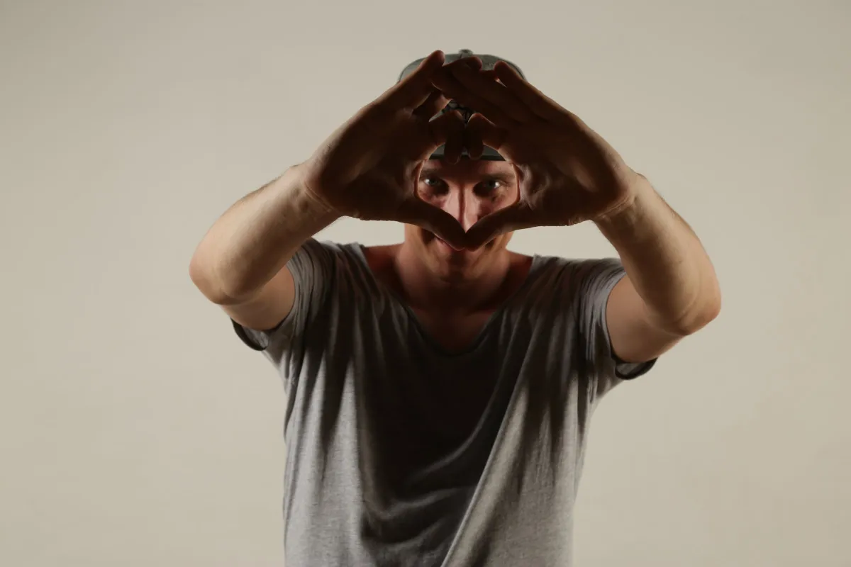 DJ EMC formt mit beiden Händen ein Herz vor dem Gesicht, heller Studiohintergrund