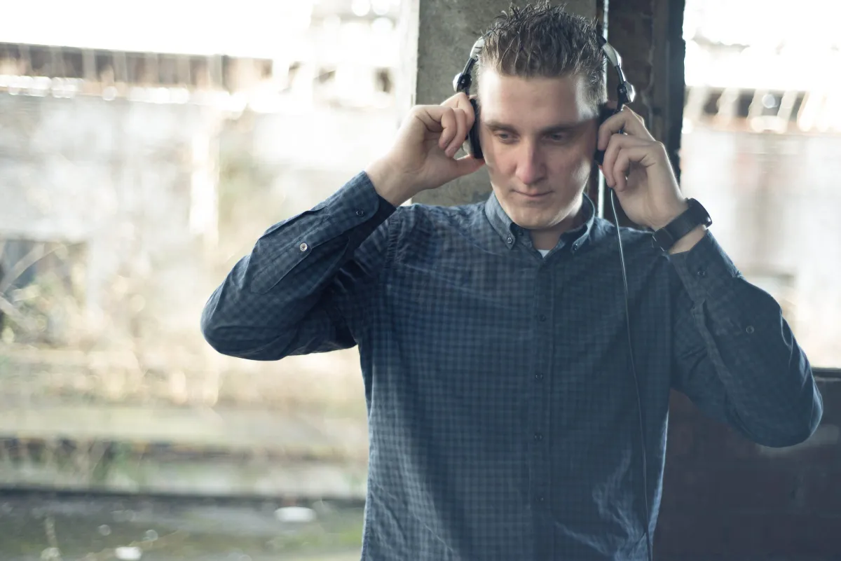DJ EMC im karierten Hemd setzt sich in einer alten Industriehalle die Kopfhörer auf