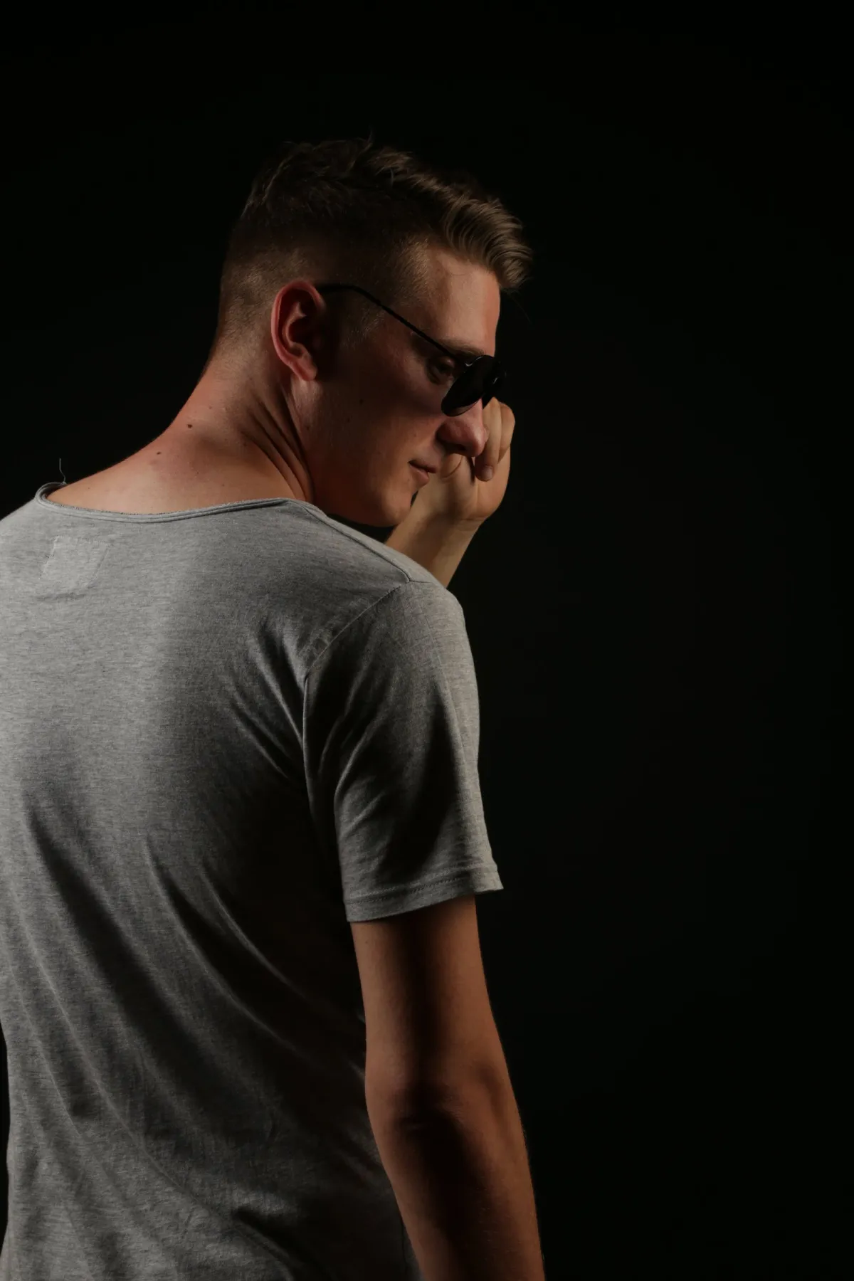 DJ EMC in Rückenansicht mit Sonnenbrille, über die Schulter blickend, vor schwarzem Hintergrund