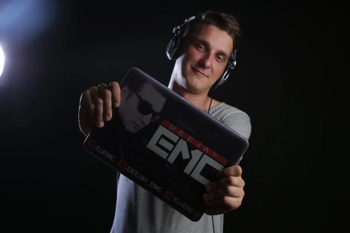 DJ EMC mit Kopfhörern hält ein Laptop-Case mit dem Logo „Deejay EMC“ in die Kamera