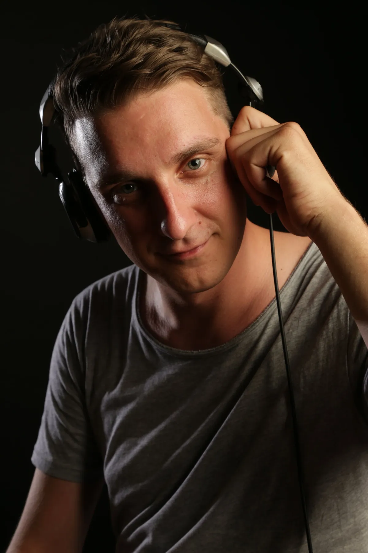 DJ EMC mit DJ-Kopfhörern am Ohr lächelt in die Kamera, dunkler Studiohintergrund