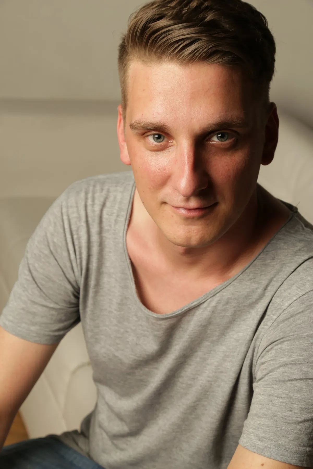 DJ EMC lächelt freundlich in die Kamera, graues Shirt, heller Raum